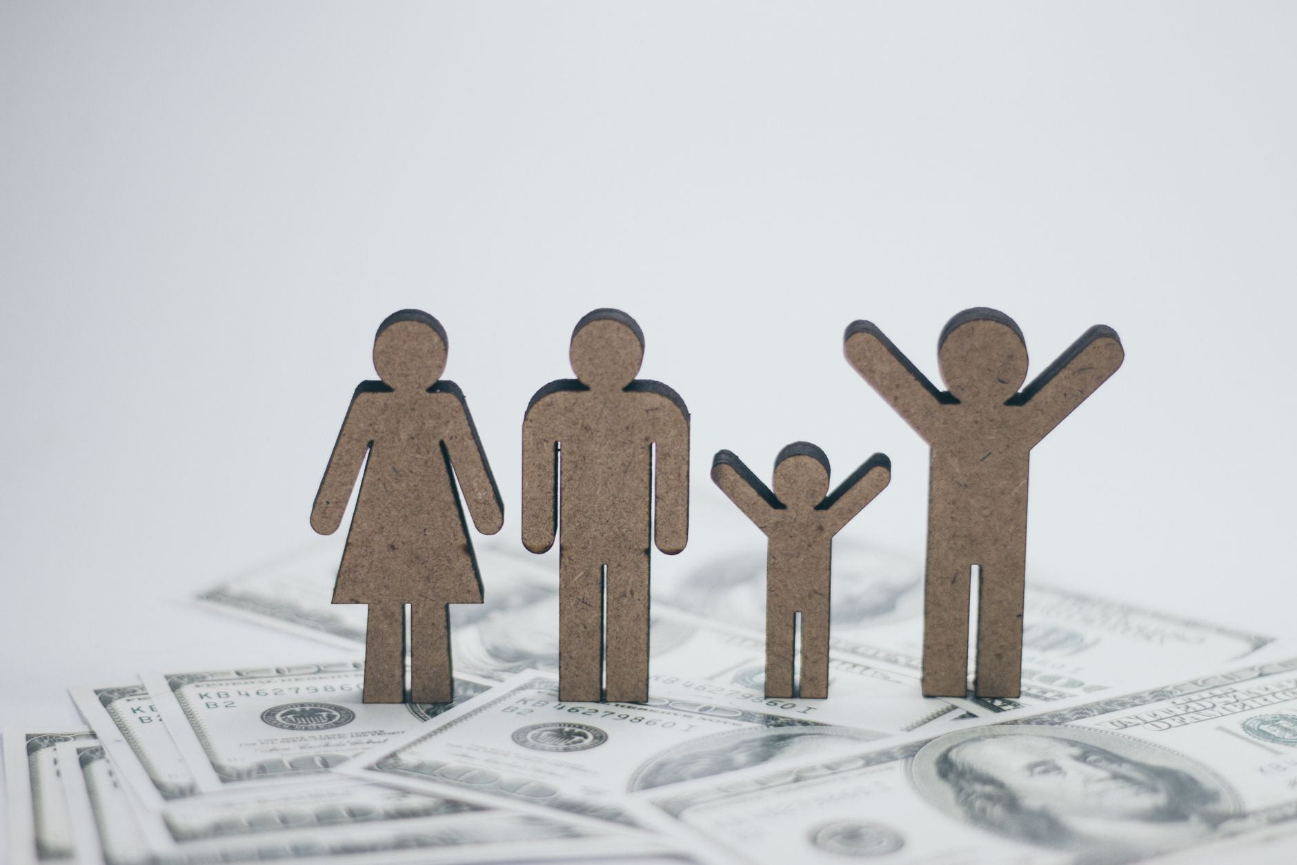 Wooden family figures standing on U.S. dollar bills, representing a household stewardship plan